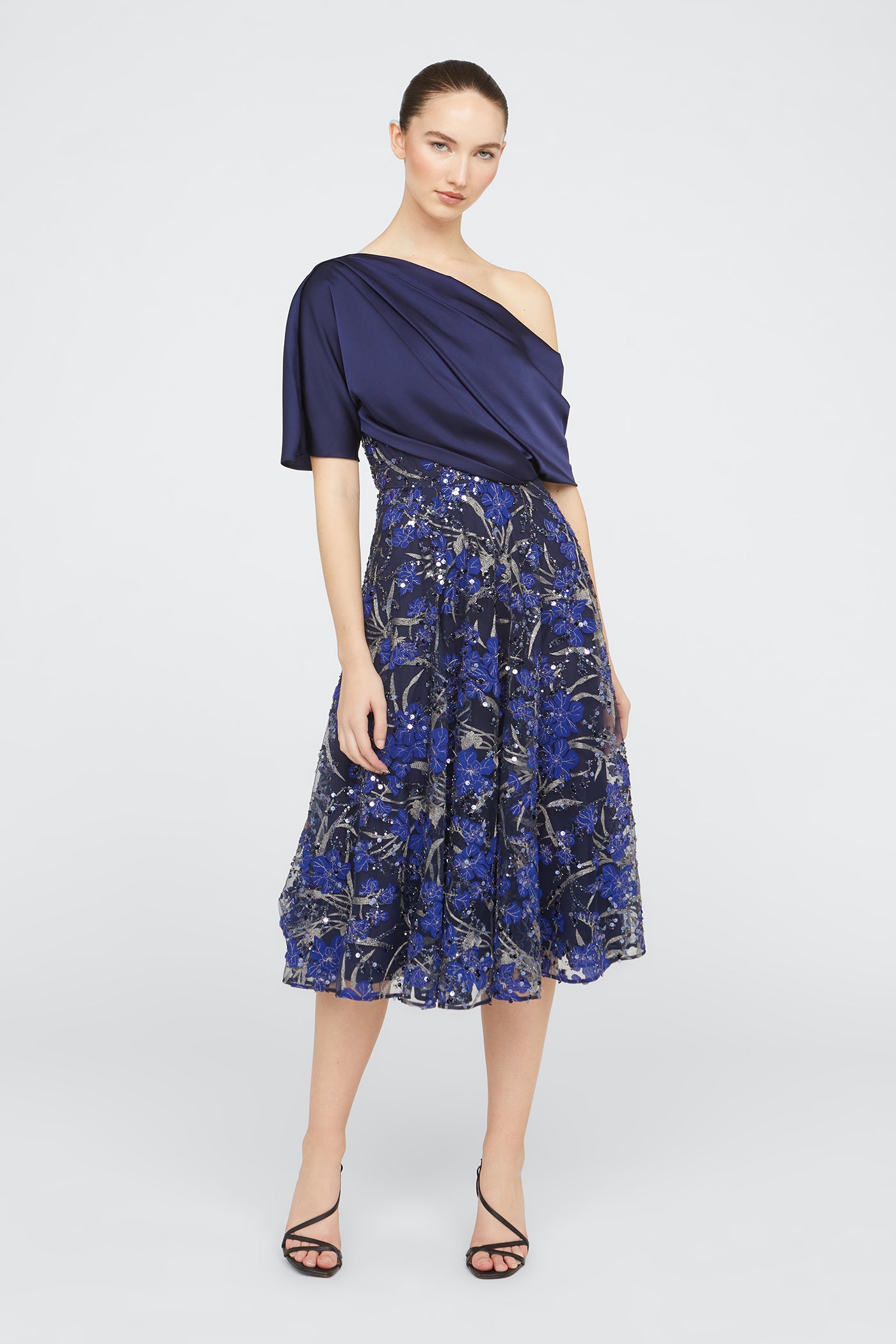 Woman wearing a navy one-shoulder dress with a floral skirt on a white background