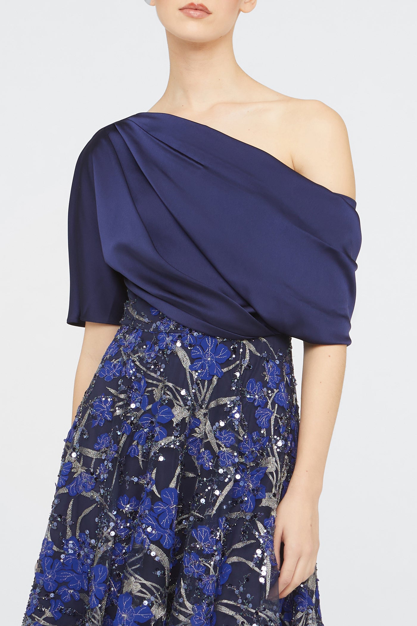 Woman wearing a blue one-shoulder dress with a floral skirt on a white background