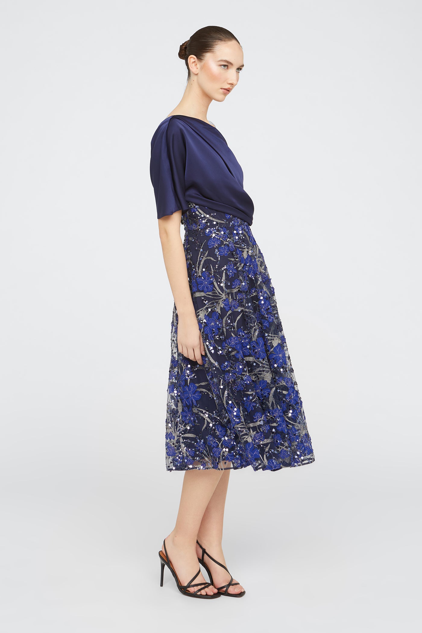 Woman wearing a dress with a navy top and blue floral skirt on a white background