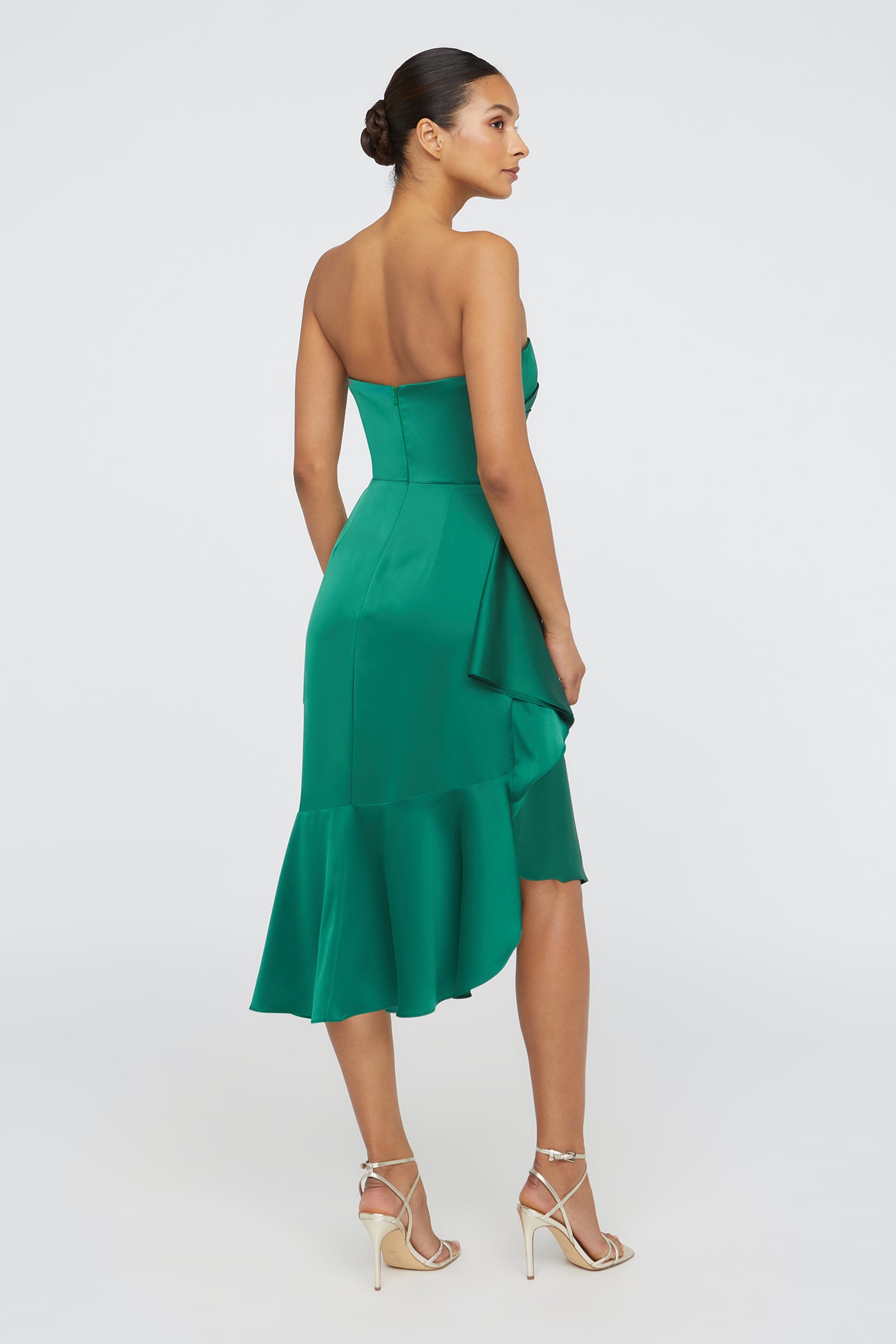 Woman wearing a green strapless dress with a ruffled hem on a white background