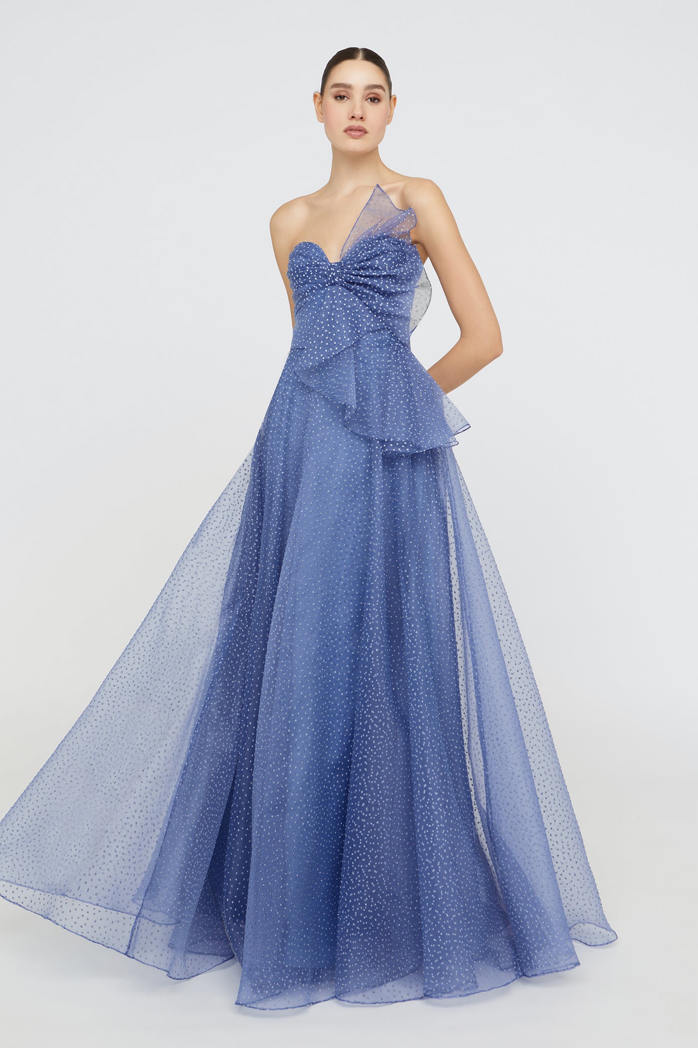 Woman wearing a blue evening gown with a bow detail on a white background