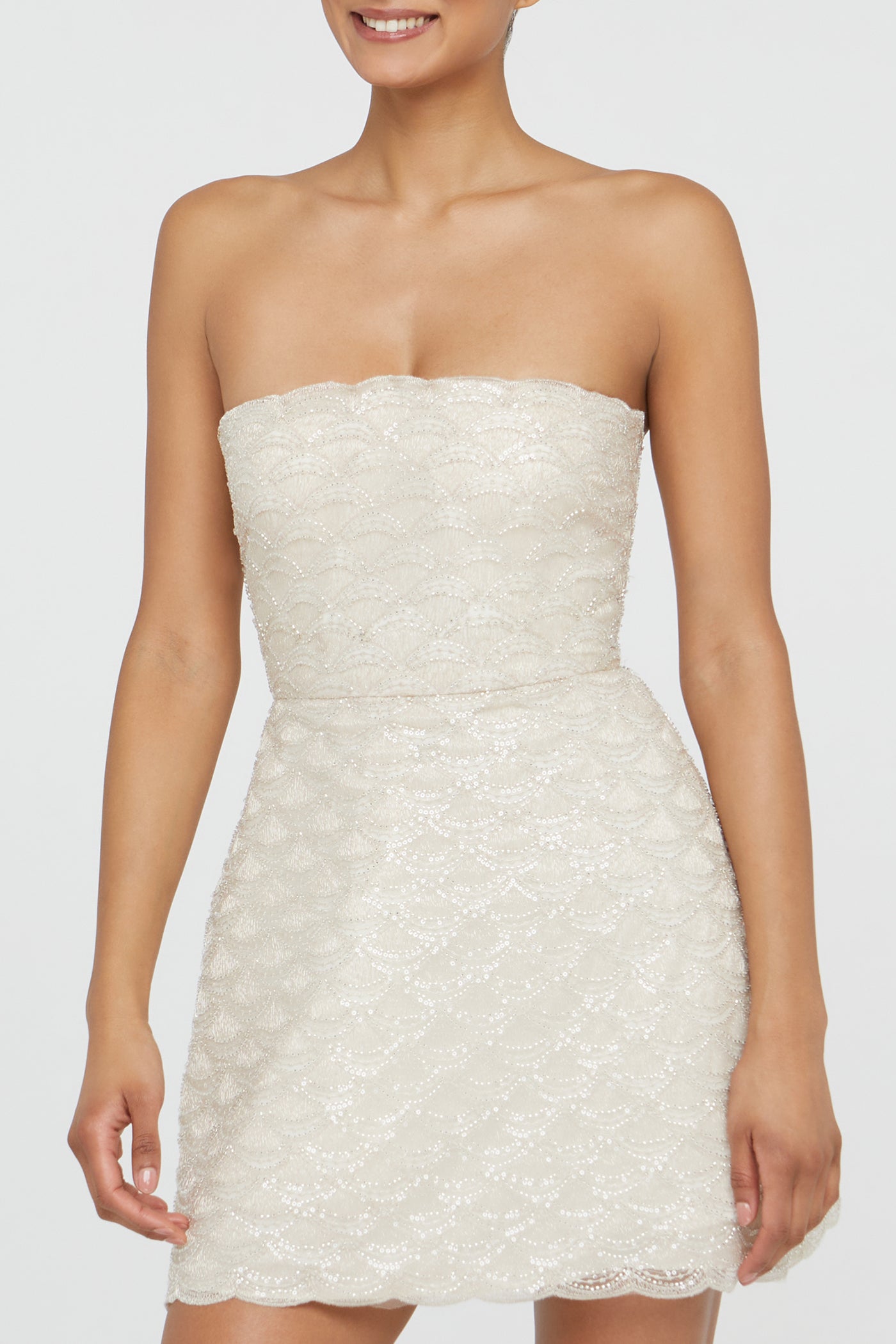 Woman wearing a strapless white lace dress on a plain background
